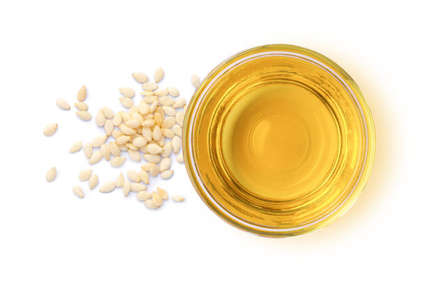Sesame Oil pictured from top in small glass bowl with white seeds on side and white background. Nutrient rich ingredient used in Vedic Tiger's products for natural hair care, skin care and nutritional supplements. 